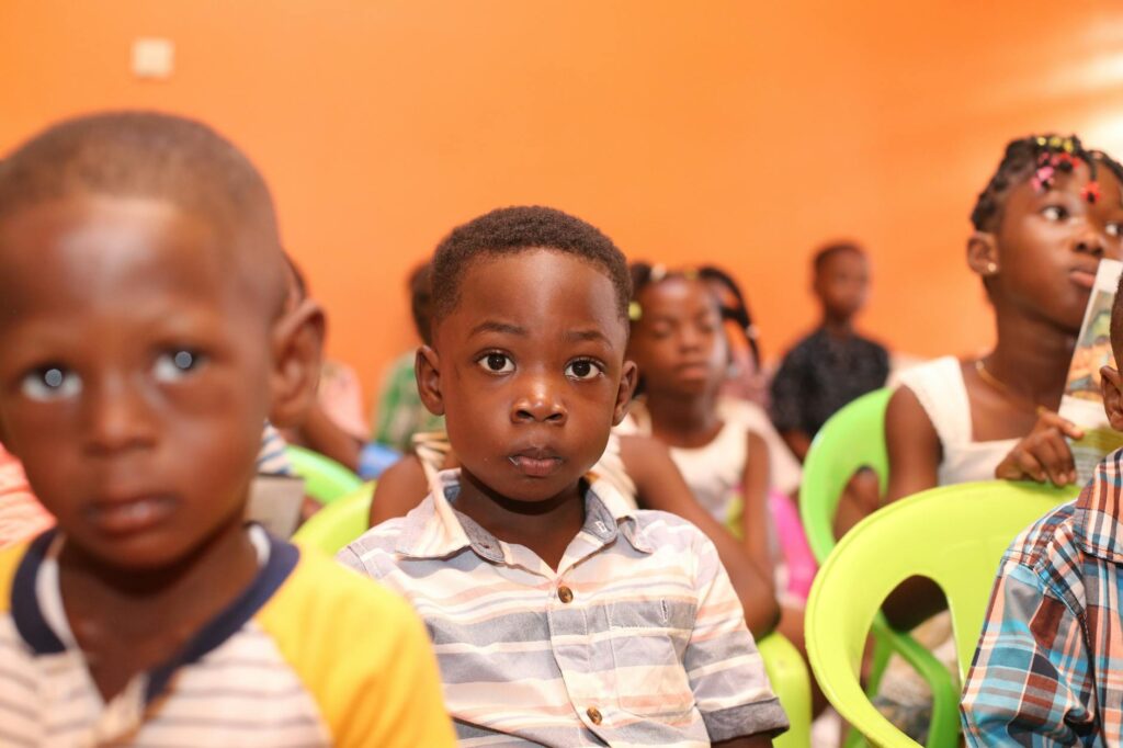 A group of children seated in a colorful classroom setting, focusing attentively.