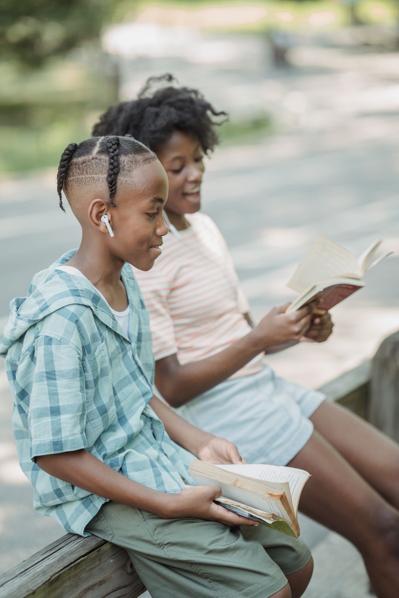 Two children reading books outdoors, enjoying a sunny day in the park.